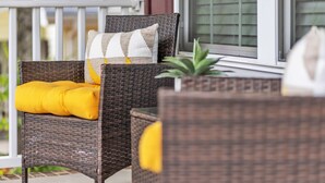 Een rieten stoel met een geel kussen en een geruit kussen op een veranda.