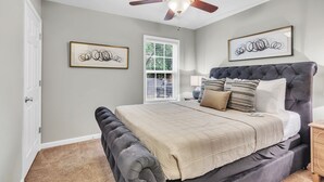 Een slaapkamer met een groot bed, een plafondventilator en twee ingelijste kunstwerken aan de muur.