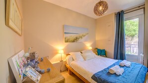 Een slaapkamer met een bed, bedlampen, een schilderij, een bureau met lamp en een raam met gordijnen.