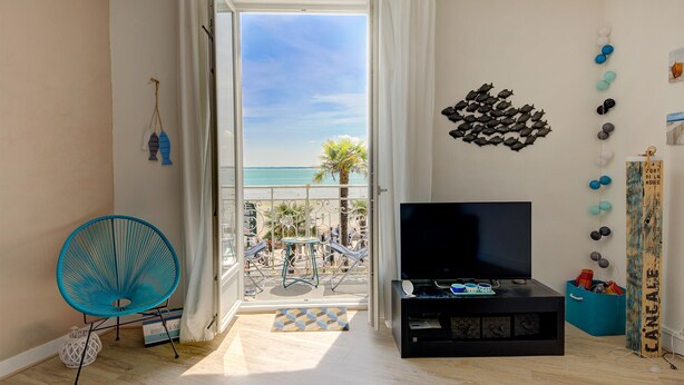 Een woonkamer met een televisie, een balkon met uitzicht op zee, en een muur versierd met een vis en een vogelbeeldhouwwerk.
