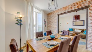 Een eetgedeelte met een houten tafel gedekt voor vier personen, een bakstenen muur en uitzicht op een balkon.