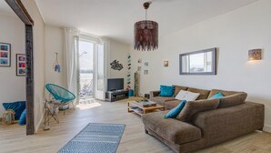 Een moderne woonkamer met een bruine bank, een blauw kamerkleed en een hanglamp.