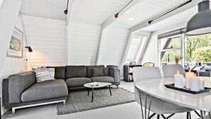 A modern loft with a grey sectional sofa, a round dining table with candles, and a large window offering a view of greenery. - Nice home in Farsø with kitchen (Farsø)