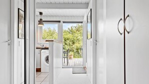 A narrow hallway with a washing machine, a dining area with a table and chairs, and a view of greenery outside. - Nice home in Farsø with kitchen (Farsø)