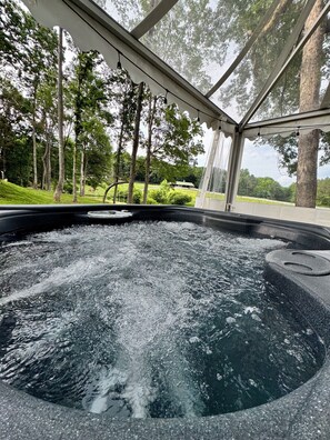 A hot tub with a glass enclosure, surrounded by trees and a grassy area. - Countryside Getaway Green UniqueDomeA/serene farm retreat (Snow Camp)
