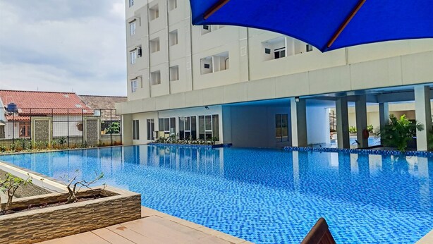 A swimming pool with a tiled edge, surrounded by a building with large windows and a blue awning. - Good Price And Homey 2Br At Loftvilles City Apartment (South Tangerang)