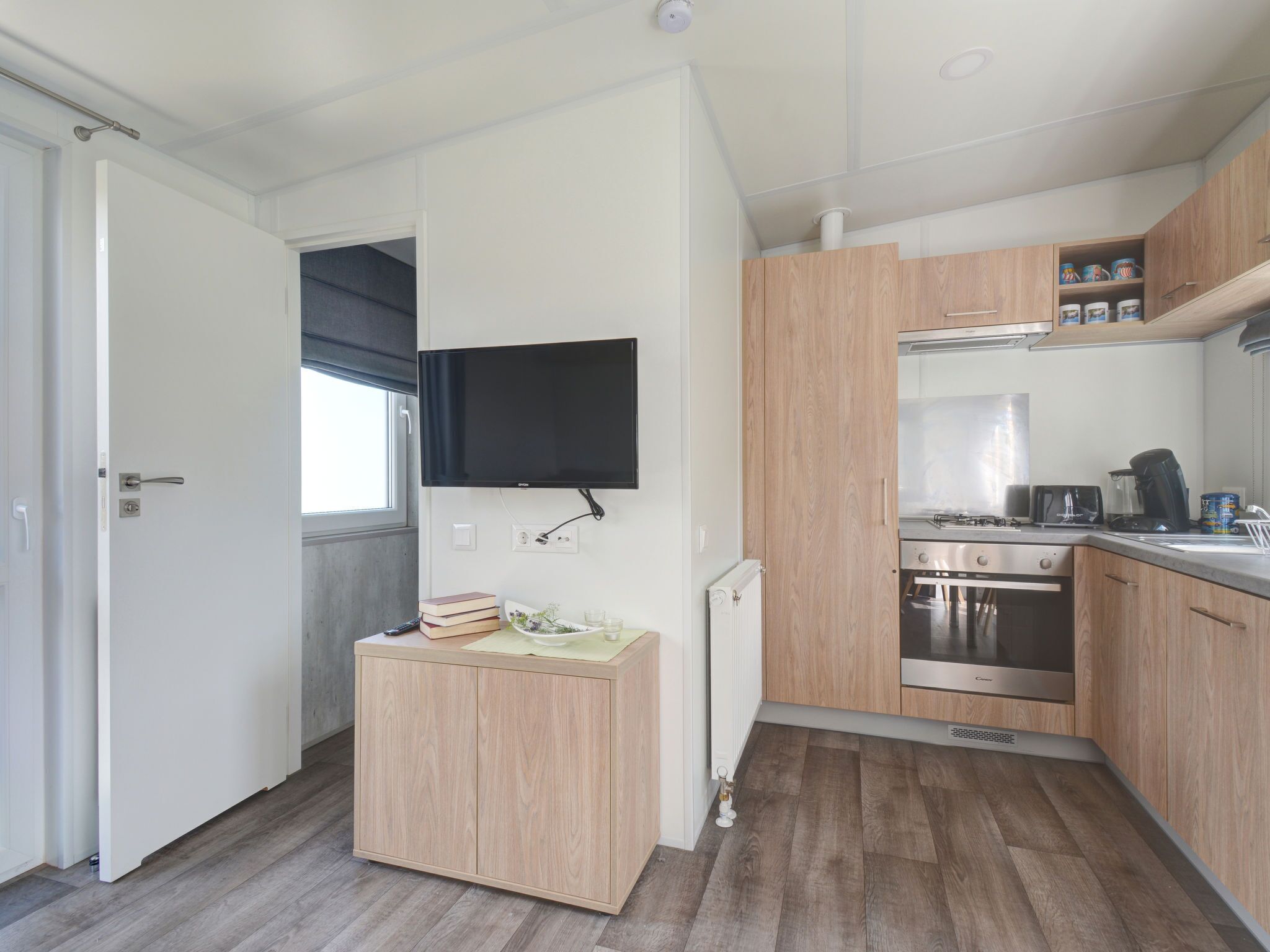 Eine kompakte Küche mit Holzausstattung, fest eingebautem Herd und einem Wand-Fernseher.