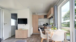 Een moderne keuken met houten kastjes, een eethoek met tafel en stoelen, een flatscreen televisie boven de werkruimte en een groot raam met uitzicht op de omgeving.