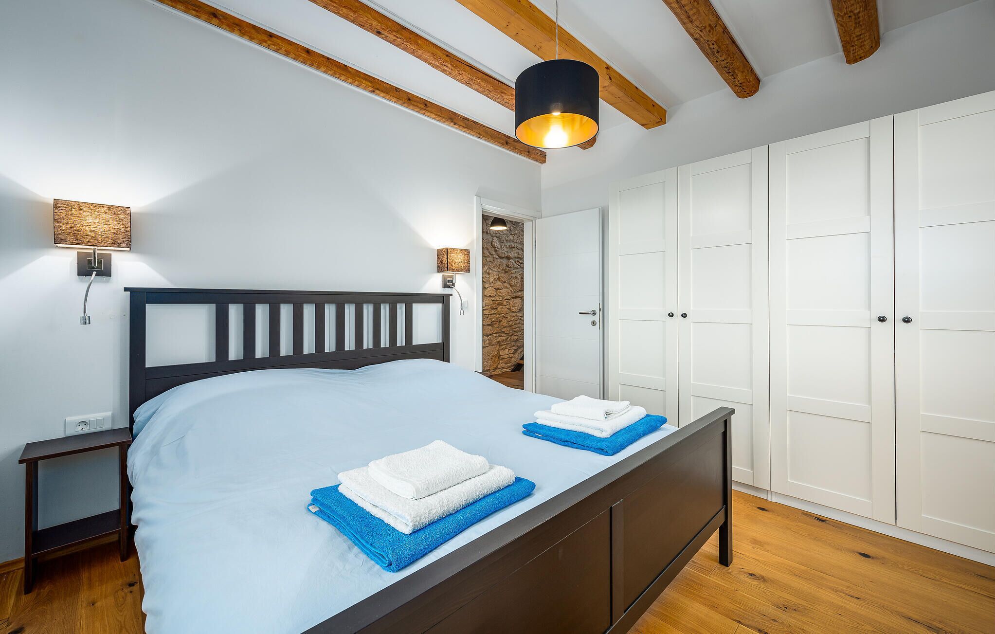 Quarto com cama, abajures, guarda-roupa e uma parede de pedra.