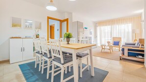 Una sala de estar moderna con comedor, que incluye una mesa de madera, sillas blancas, un sofá y un ventanal con cortinas.