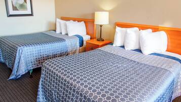 A hotel room with two beds, each with a blue patterned bedspread, a wooden headboard, and white pillows. There is a nightstand with a lamp between the beds.