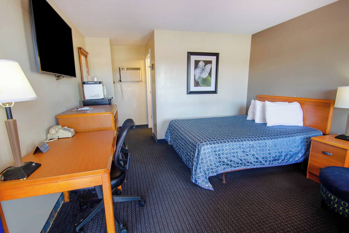 Una habitación de hotel con cama, escritorio, silla y televisor.