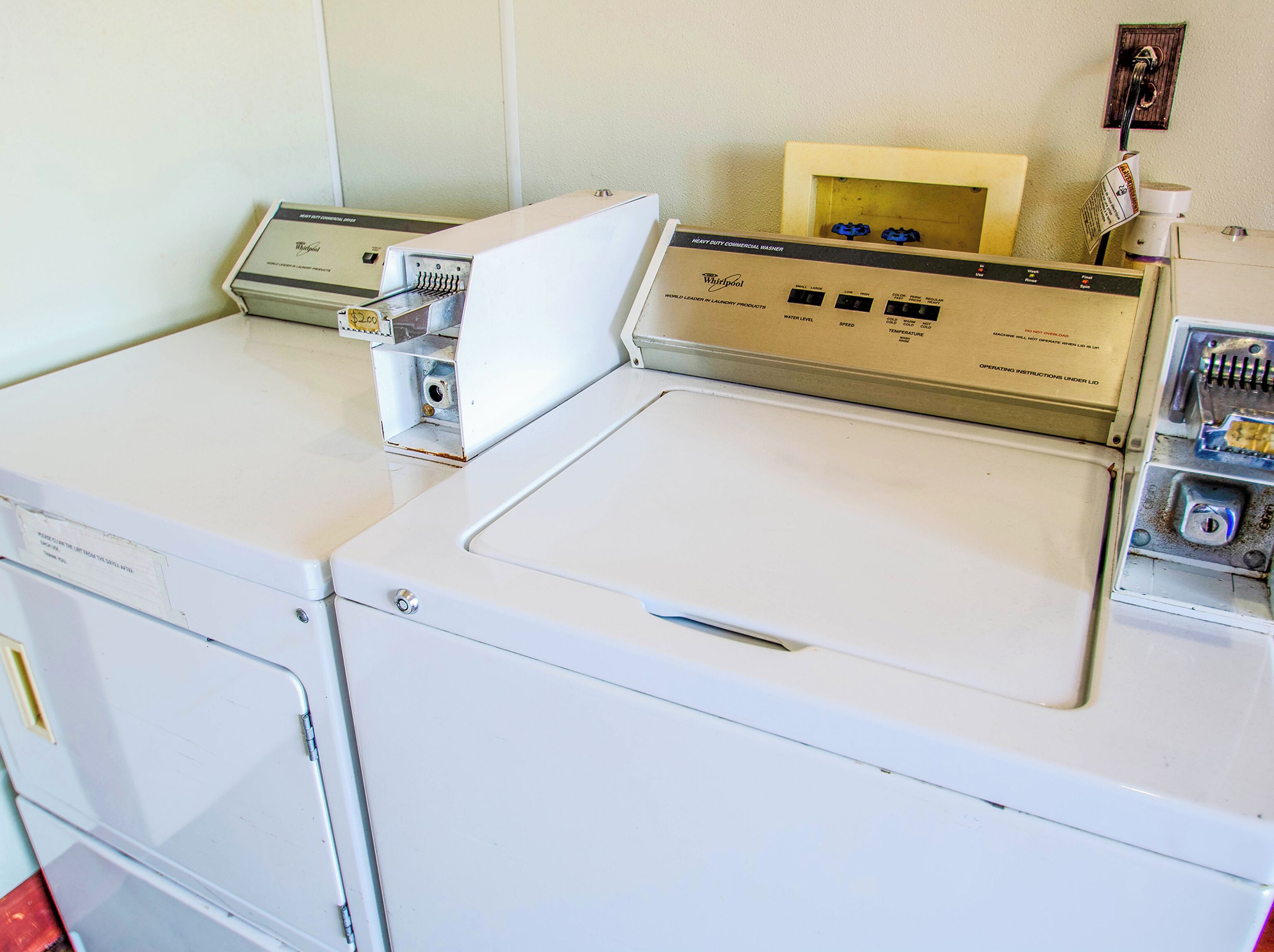 Un appareil combiné lave-linge et sèche-linge à chargement frontal, doté d’un panneau de commande, d’une petite étagère en bois et d’une machine à café fixée au mur.