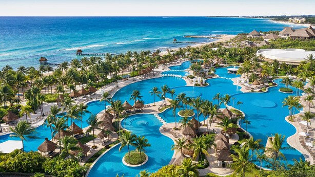 Un complejo turístico con varias piscinas, palmeras y una playa.