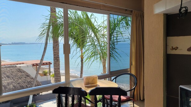 Une pièce avec une grande fenêtre donnant sur une plage, une table avec un livre et une chaise.