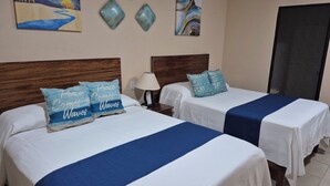 A hotel room with two beds, each with a blue bedspread and matching pillows. There are wall art pieces above the beds and a door to the right. - Dos recamaras en la playa conveniente (bucerias)
