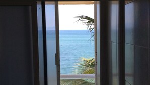 Uitzicht vanuit een kamer met een schuifglazen deur naar een balkon met uitzicht op zee.
