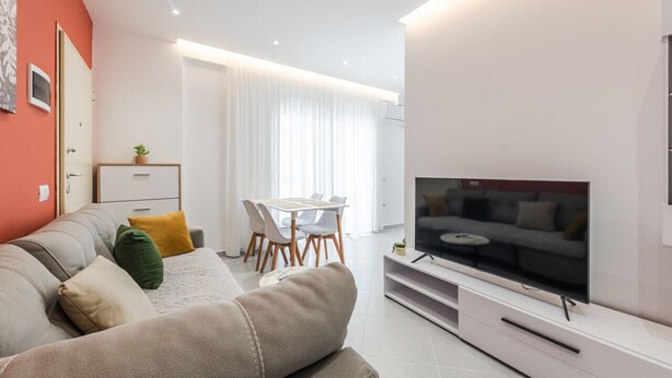 Uma sala de estar moderna com sofá, televisão e área de jantar.