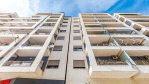 Um hotel com vários andares, design moderno, com varandas e céu azul ao fundo.