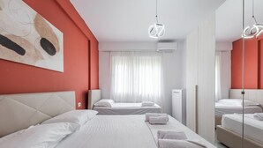 A hotel room with a large bed, two smaller beds, a mirror, and a ceiling light fixture.