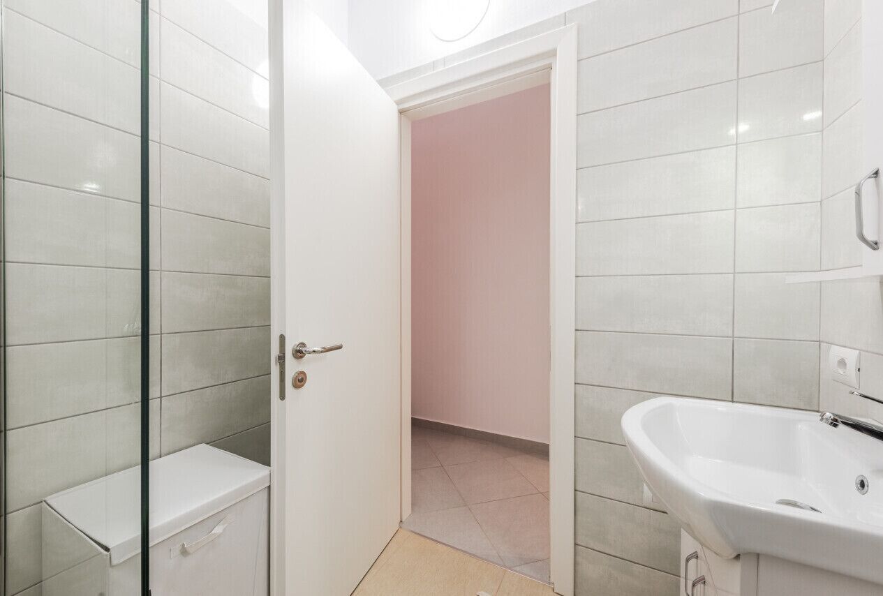 A bathroom with a glass shower enclosure, a white sink, and a pink wall.