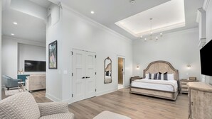 Un dormitorio espacioso con una cama grande, una zona de estar con una butaca y reposapiés, un televisor y un espejo.