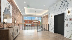 Un lobby moderno con piso de madera, pared de ladrillo con un retrato grande, una escalera y pared de mármol con ascensor.