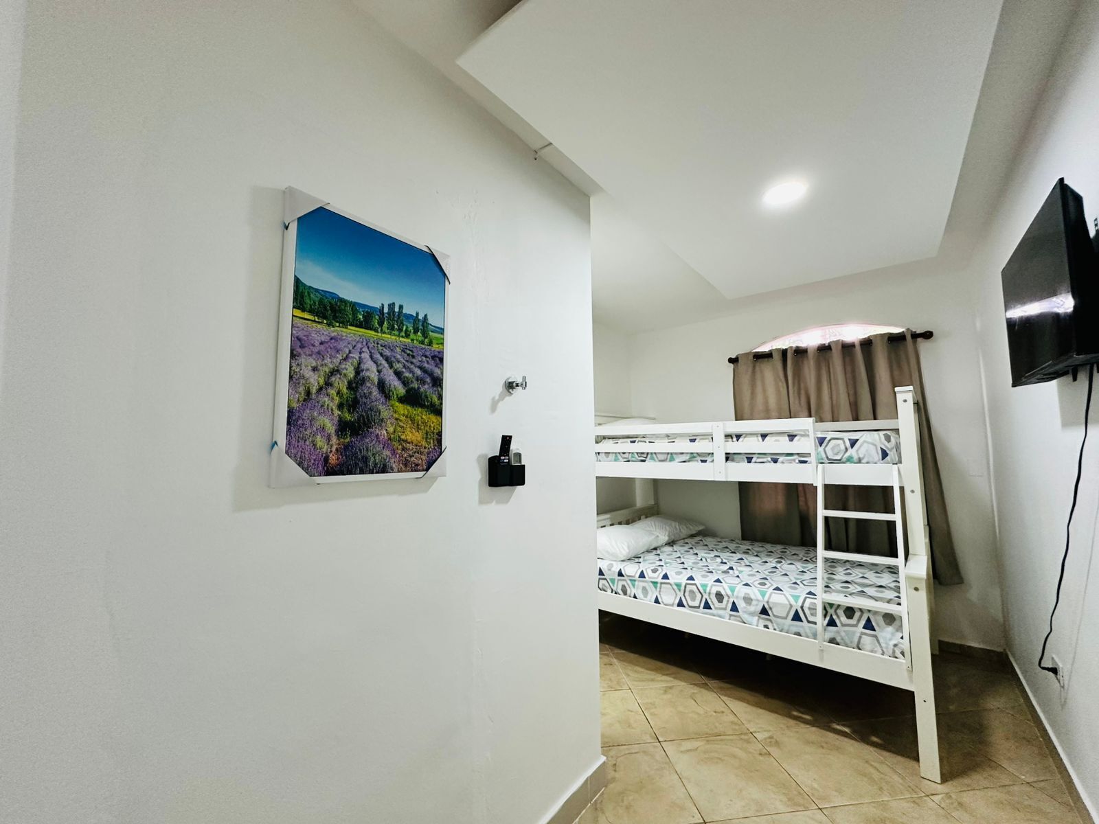 Een kamer met een stapelbed, een wandtelevisie en een foto van een lavendelveld aan de muur.
