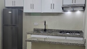 A kitchen with white cabinets, a granite countertop, a stainless steel refrigerator, and a pendant light. - Lila House (Samaná)