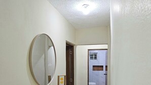 A hallway with a marble floor, a wooden shelf with a mirror, and a door leading to a bathroom. - Lila House (Samaná)