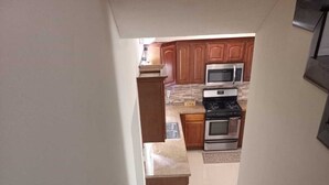 Un escalier menant à une cuisine équipée de meubles en bois, d’un four à micro-ondes et d’un four traditionnel.