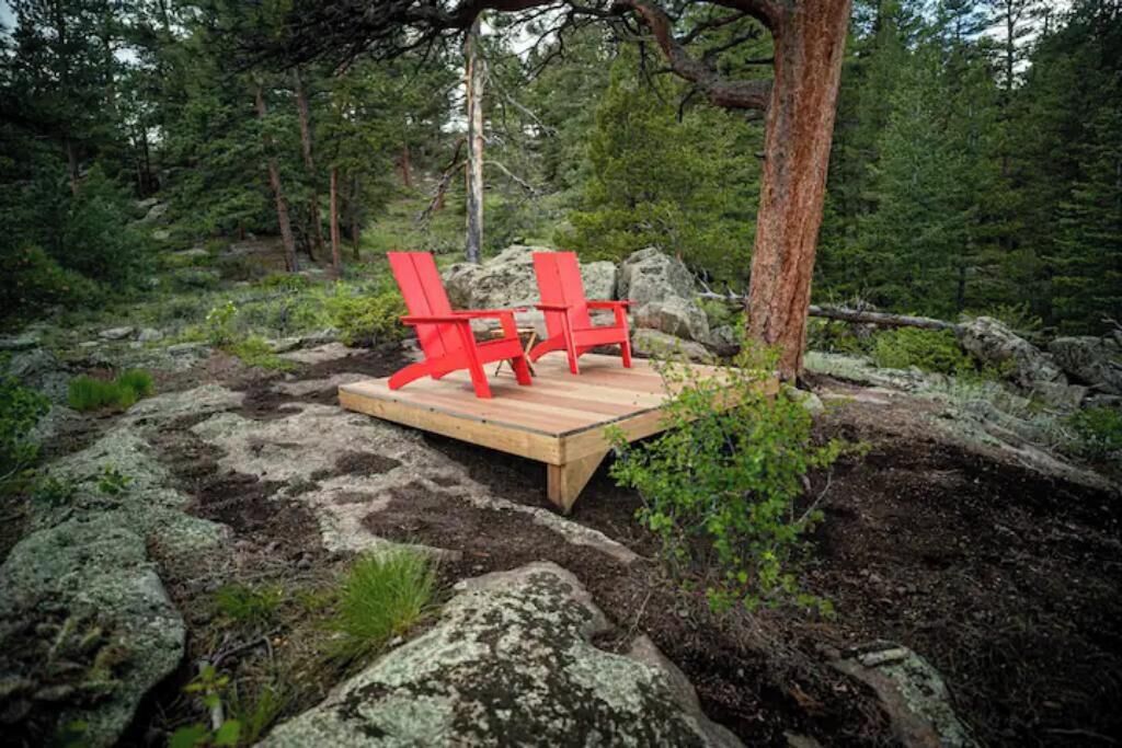 Puinen terassi, jossa on kaksi punaista Adirondack-tyylistä tuolia, metsäisessä ympäristössä.