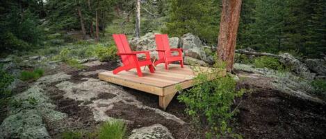 Puinen terassi, jossa on kaksi punaista Adirondack-tyylistä tuolia, metsäisessä ympäristössä.
