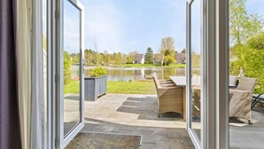 Eine Terrasse mit Korbmöbeln und Blick auf einen See sowie Häuser in der Ferne.