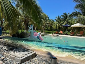 A pool area with clear water, lounge chairs, and a decorative unicorn float.