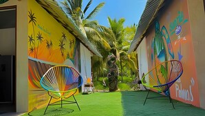 Un étroit couloir extérieur aux murs ornés de peintures murales colorées, avec deux chaises vives et une petite statue au centre.
