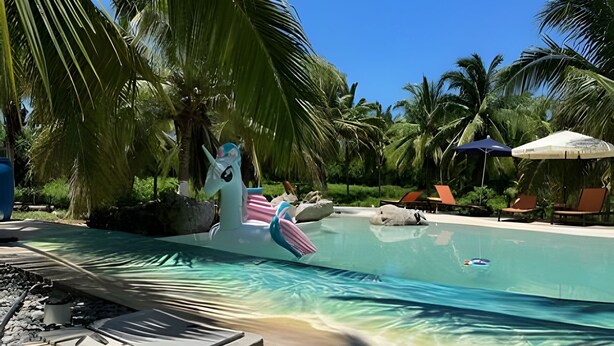 Area piscina con lettini, ombrelloni e una statua decorativa a forma di unicorno.