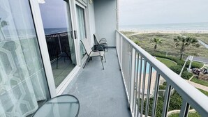 A balcony with a view of the beach, two chairs, and a glass table. - Two Bedroom One Bath Beachfront Condo (South Padre Island)