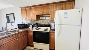A kitchen with wooden cabinets, a white refrigerator, a stove, and a microwave. - Two Bedroom One Bath Beachfront Condo (South Padre Island)