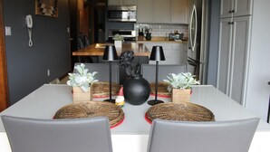 Una cocina moderna con armarios blancos, electrodomésticos de acero inoxidable y un comedor con mesa blanca y sillas grises.