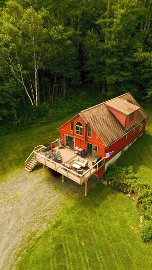 A two-story house with a deck, surrounded by dense forest.
