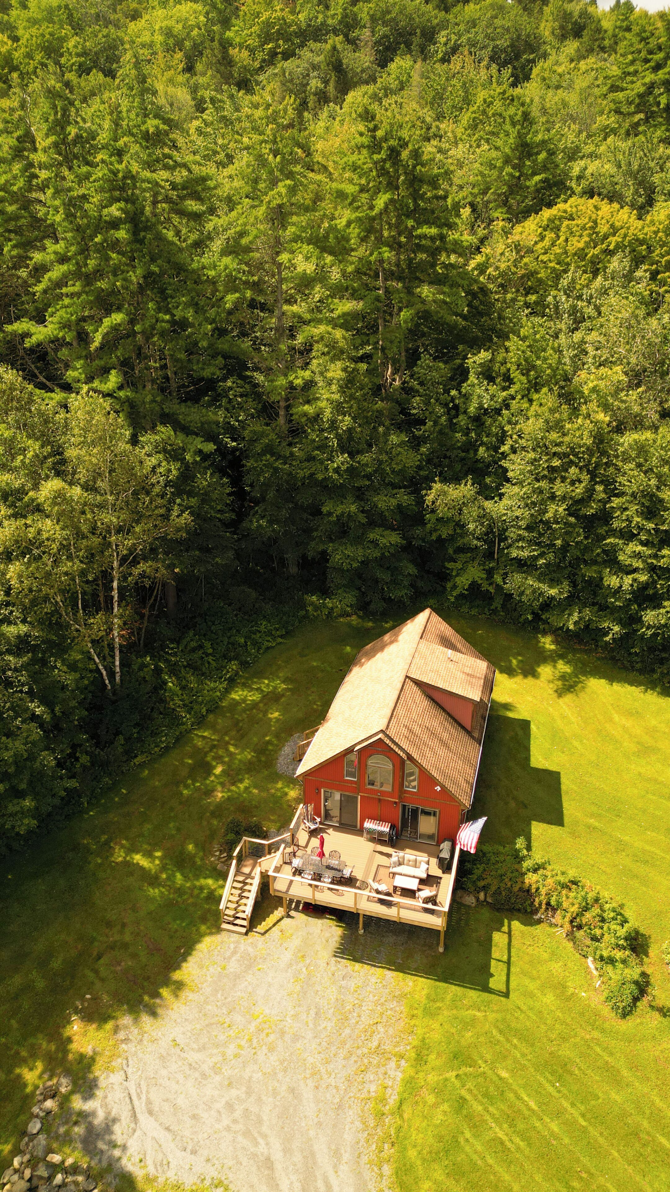 Eine Vogelperspektive auf eine rote Holzhütte mit einer Terrasse, umgeben von dichtem Wald.
