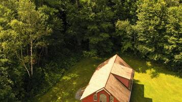 Eine Vogelperspektive auf eine rote Holzhütte mit einer Terrasse, umgeben von dichtem Wald.