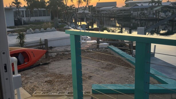 A view of a waterfront area with a wooden deck, a kayak, and a palm tree.