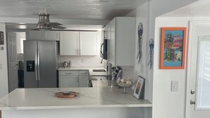 A modern kitchen with white cabinetry, a stainless steel refrigerator, a marble countertop, and a built-in island with bar stools.