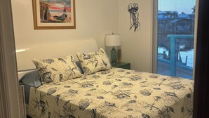 A bedroom with a bed, a nightstand, a lamp, a framed picture, and a window with a view.