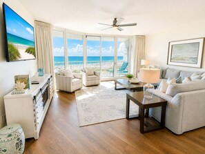 A spacious living room with a view of the ocean, a ceiling fan, and a large window with curtains.