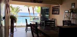 A room with a view of the ocean, a dining table, chairs, a bookshelf, and a plant.