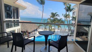 Ein Balkon mit Pool, Stühlen und Blick auf das Meer und Palmen.