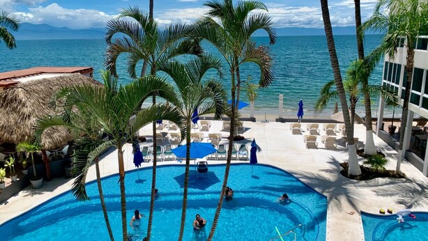 Ein Poolbereich mit mehreren Schwimmbecken, Liegestühlen und Palmen.